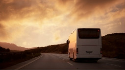 bus driving along open road at sunset